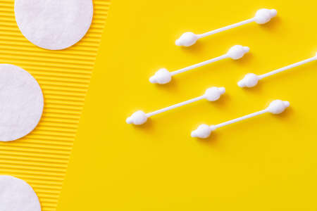 top view of hygienic ear sticks and cosmetic cotton pads on yellow textured background