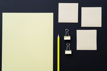 top view of blank paper near sticky notes, pencil and fold back clips on black