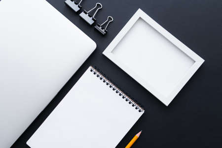 flat lay of fold back clips near notebook, frame and laptop on blackの写真素材