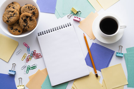 top view of bowl with biscuits near cup of coffee and stationery on white
