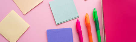 top view of colorful pens near bright notebook and blank paper notes on pink, banner