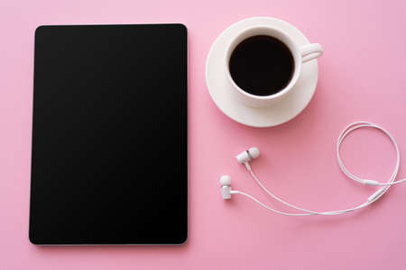 top view of digital tablet with blank screen near cup of coffee and wired earphones on pink