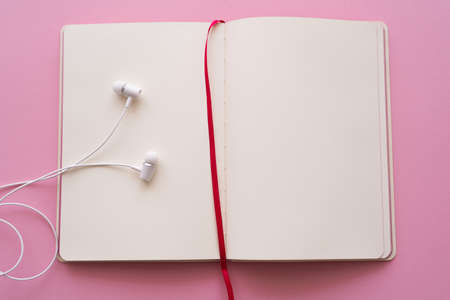 top view of open notebook and wired earphones on pinkの写真素材