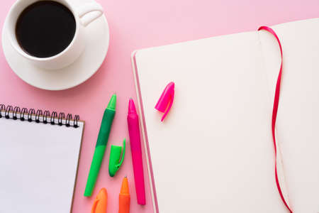 top view of colorful pens near blank notebooks and cup of coffee on pinkの写真素材