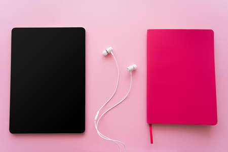 top view of digital tablet with blank screen near earphones and bright notebook on pinkの写真素材