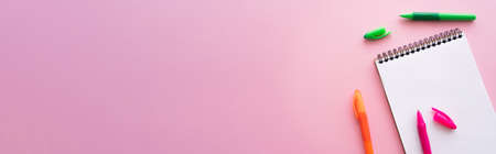 top view of colorful and bright pens near blank notebook on pink, bannerの写真素材