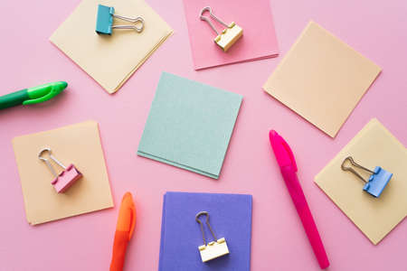 flat lay of fold back clips on colorful paper notes near pens on pinkの写真素材