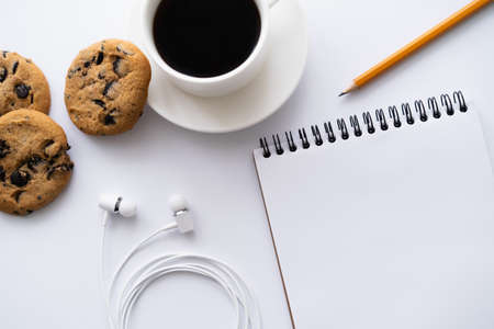 top view of cup of coffee near chocolate chip cookies, stationery and wired earphones on whiteの写真素材