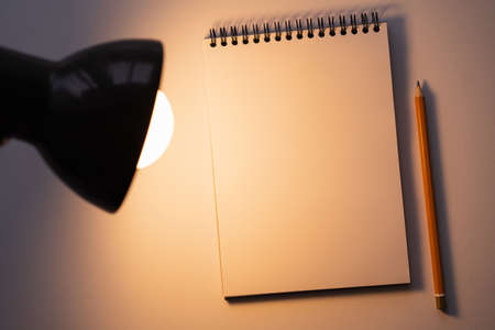 top view of blank notebook near pencil and turned on lamp on whiteの写真素材