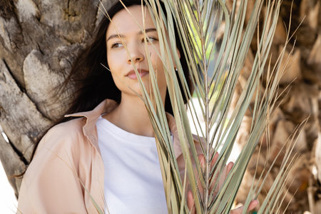 brunette woman looking away near dry palm leaves