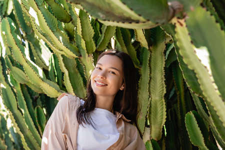 cheerful brunette woman looking at camera near green succulentsの写真素材