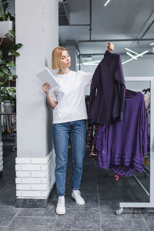 Saleswoman holding digital tablet and clothes in second handの写真素材