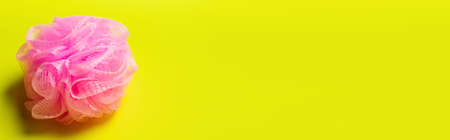top view of pink exfoliating shower puff on yellow background with copy space, banner
