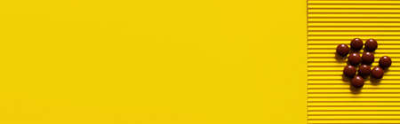 top view of pile with brown round shape pills on yellow textured background, banner