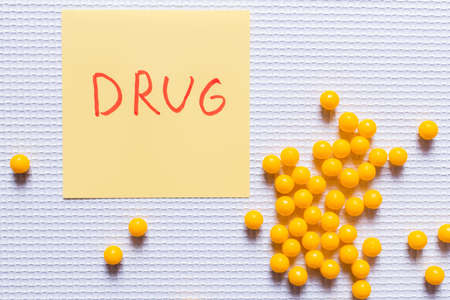 top view of yellow round shape pills near paper note with drug lettering on white textured...