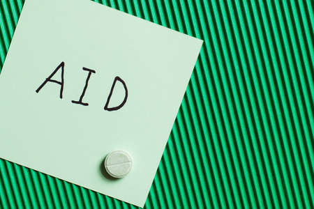 top view of round shape pill near paper note with aid lettering on textured green backgroundの写真素材