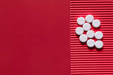 top view of pile with white round shape pills on crimson textured background