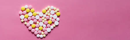 flat lay view of different round pills in shape of heart on pink background, bannerの写真素材