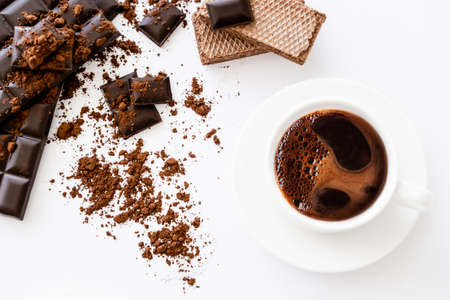 Top view of coffee in cup, waffles and dark chocolate on white background