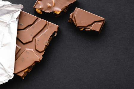 Top view of delicious milk chocolate with nuts in foil on black backgroundの写真素材