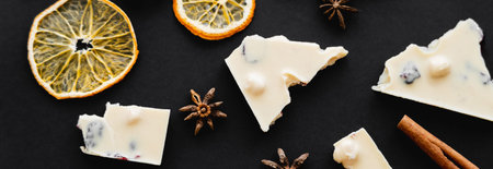 Top view of dry orange slices, spices and white chocolate on black background, banner