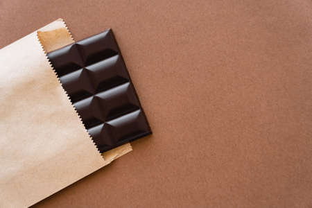 Top view of dark chocolate bar in craft package on brown backgroundの写真素材