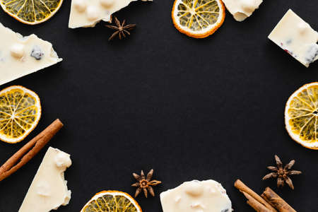 Top view of frame from white chocolate, dry orange slices and spices on black backgroundの写真素材
