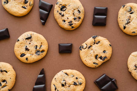 Top view of chocolate pieces near cookies on brown background