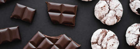 Top view of chocolate near biscuits on black background, banner