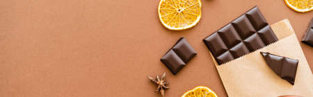 Top view of anise, dry orange slice and chocolate in craft package on brown background, bannerの写真素材