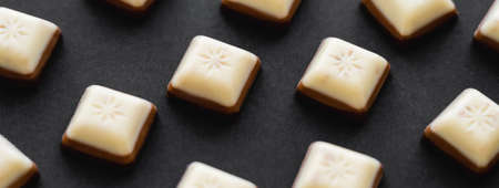 Close up view of white and milk chocolate pieces on black surface, banner