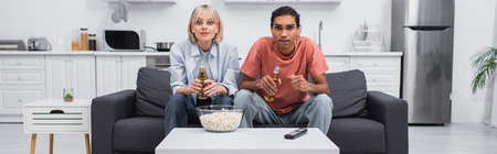 young multiethnic couple cheering while watching sport match in living room, banner