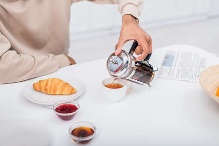 cropped view of african american man pouring tea in cup