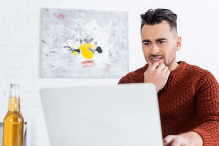 worried bookmaker looking at laptop near blurred bottle of beerの写真素材
