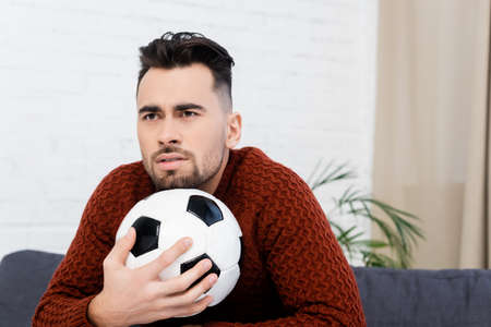 worried sports fan with soccer ball watching championship at home