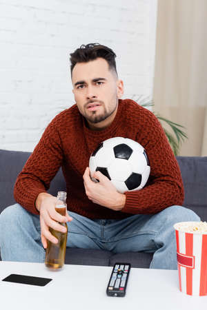 tense sports fan with soccer ball and beer watching championship on tv at home