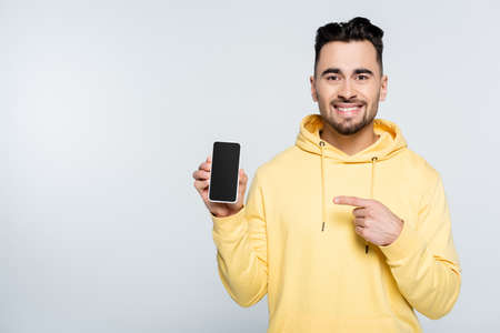 smiling man pointing at smartphone with blank screen isolated on grey