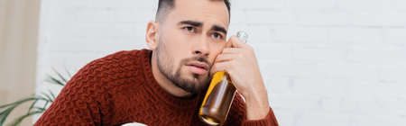 depressed bookmaker with bottle of beer looking away at home, banner