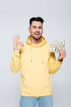 excited bookmaker holding dollars and showing okay sign isolated on grey