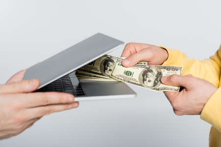 cropped view of gambler holding dollars near laptop isolated on grey