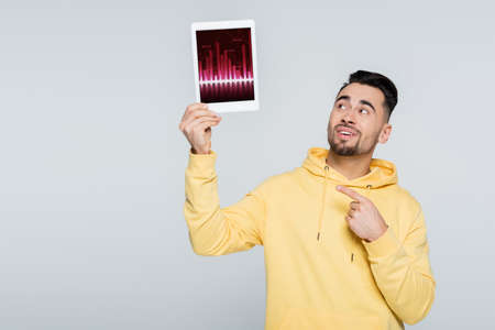 smiling man pointing at digital tablet with charts isolated on grey