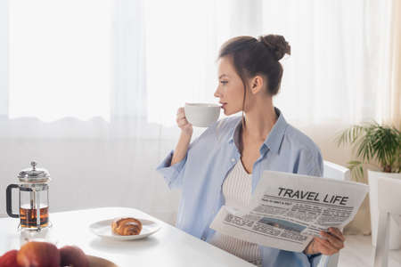 young woman with travel life newspaper drinking tea near tasty croissant