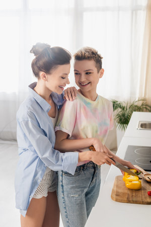 cheerful pangender person helping partner cutting bell pepper in kitchenの写真素材