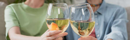 partial view of blurred pangender couple clinking glasses with white wine, banner