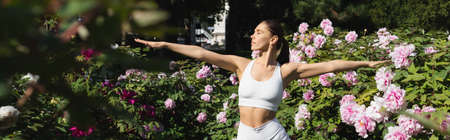 fit woman in white sports bra exercising with outstretched hands in park, banner