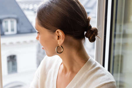 woman in ring earring looking out window at home