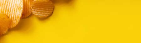 top view of wavy and salty potato chips on yellow, banner