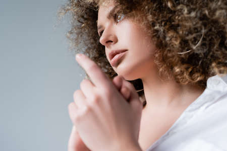 Low angle view of pretty curly woman looking away isolated on grey