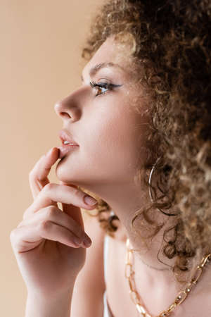 Side view of young curly model touching lip isolated on beige