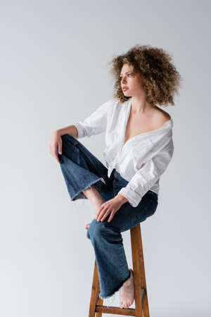 Young curly and barefoot model posing on chair isolated on whiteの写真素材